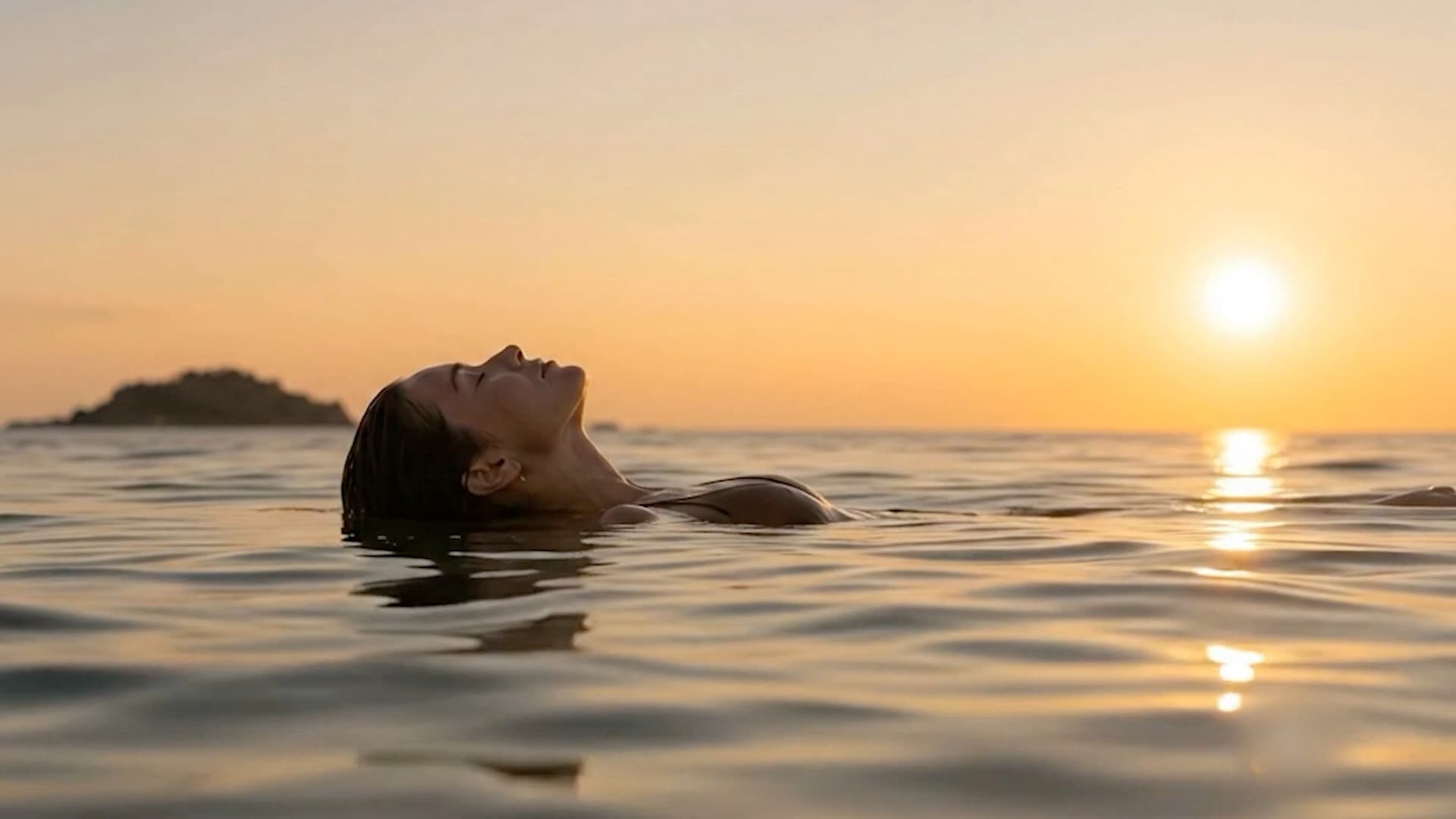 A woman floating on her back in the sea at sunset